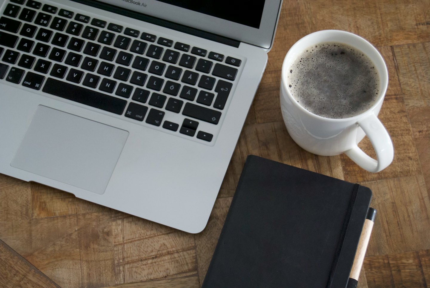 Un computer portatile, un taccuino e un caffè su una scrivania di legno.